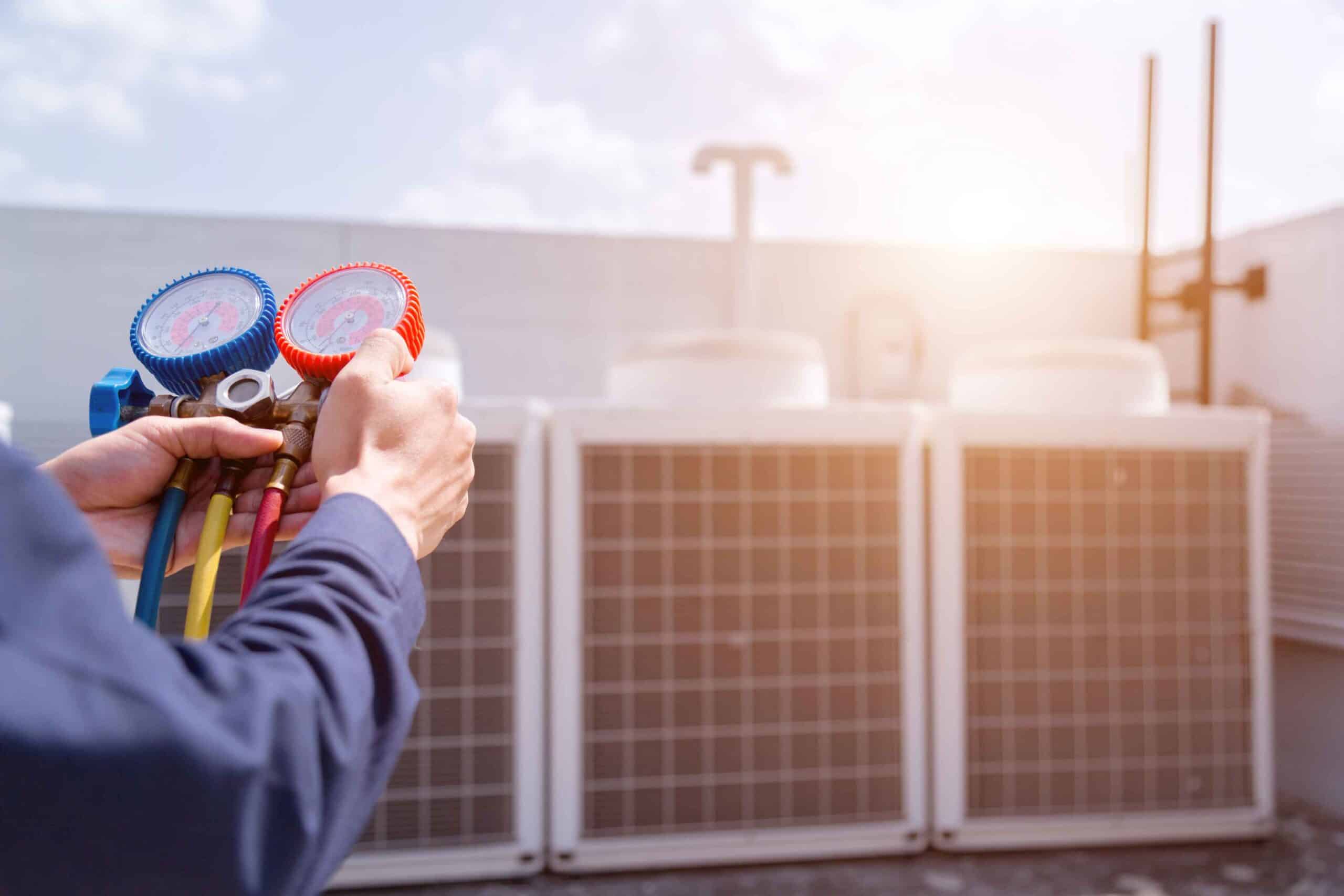 HVAC technician holding pressure gauges near rooftop air conditioning unit