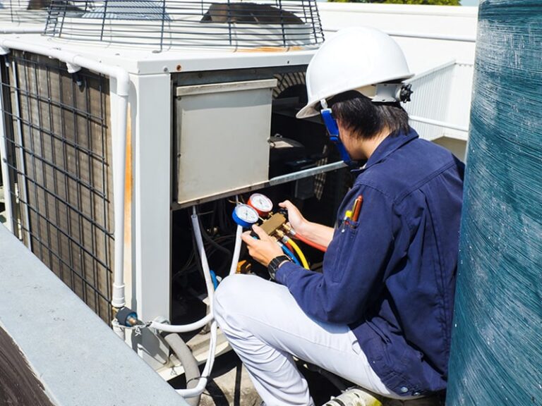 Technician servicing commercial HVAC unit with diagnostic gauges on rooftop