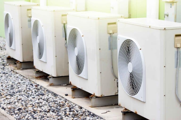 Row of outdoor HVAC air conditioning units with condensers on gravel pad