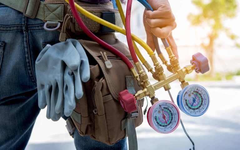 HVAC technician holding gauges and hoses with tool belt and work gloves