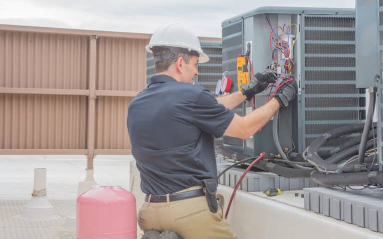 Technician in hard hat servicing HVAC unit on commercial rooftop
