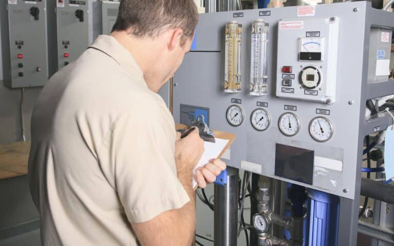 Technician inspecting industrial control panel with gauges and monitoring equipment