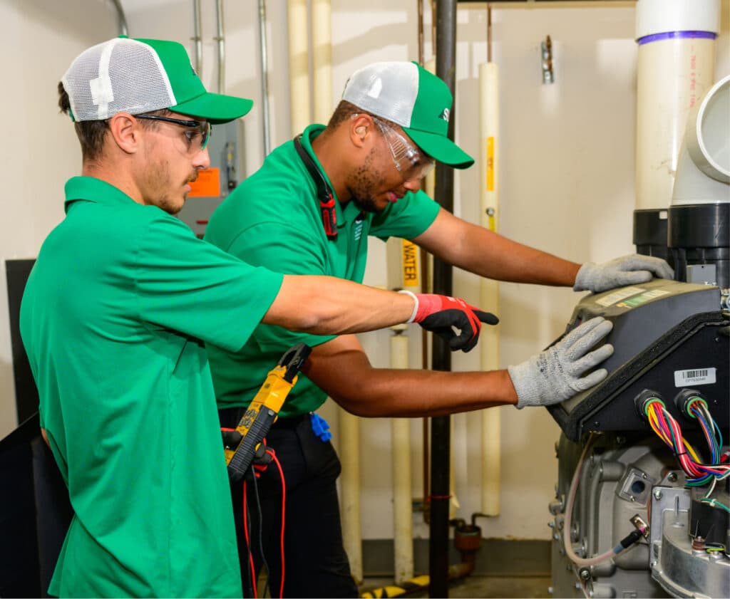 Two HVAC technicians in green uniforms servicing commercial equipment