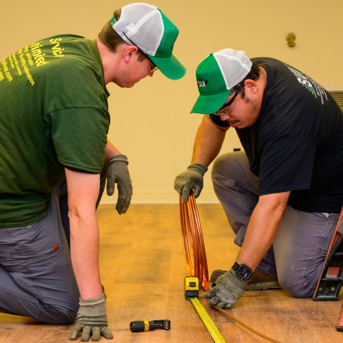 Two HVAC technicians measuring copper tubing during commercial system installation