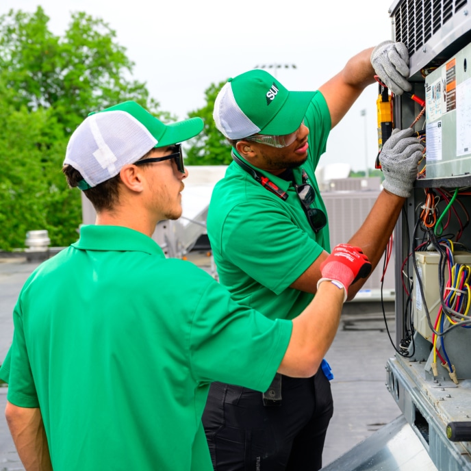 Two HVAC technicians servicing commercial rooftop equipment